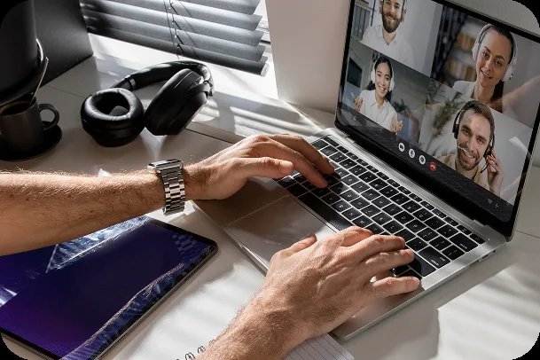 Mains sur un ordinateur portable pendant une réunion en visio, un casque et une tablette posés à côté